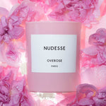 Pink candle labeled 'Nudesse' surrounded by pink roses.