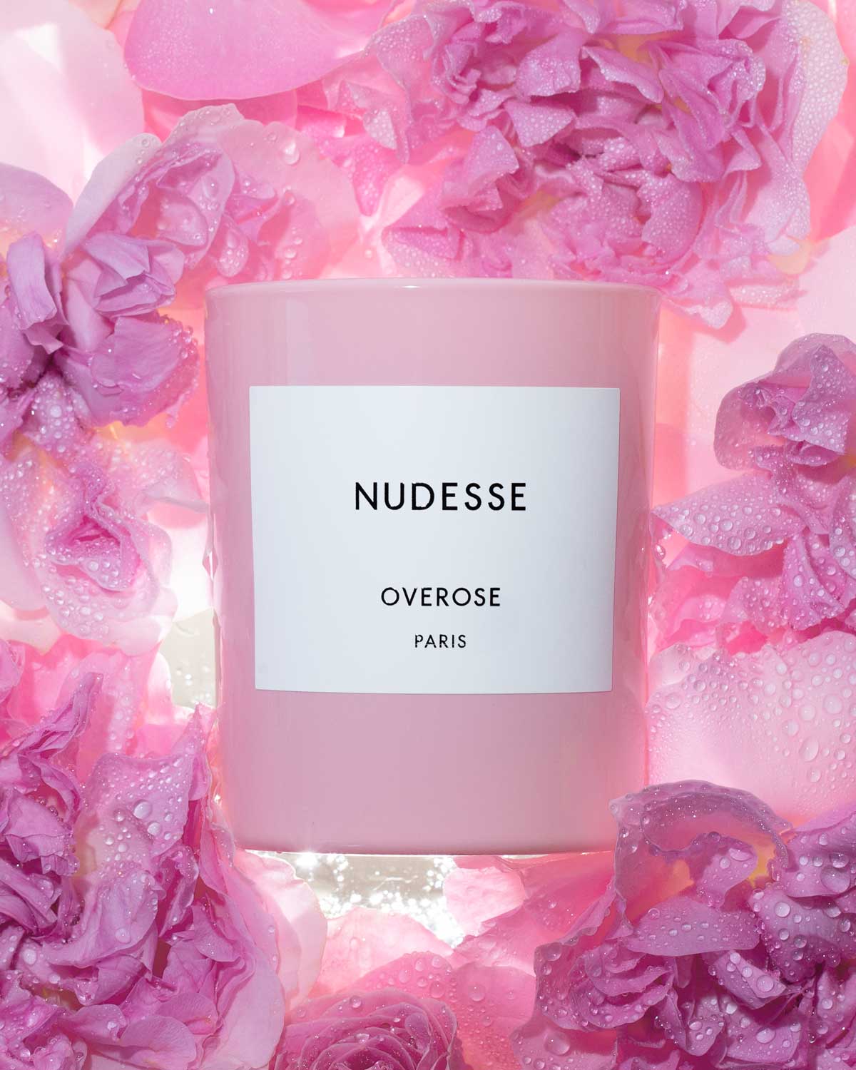 Pink candle labeled 'Nudesse' surrounded by pink roses.