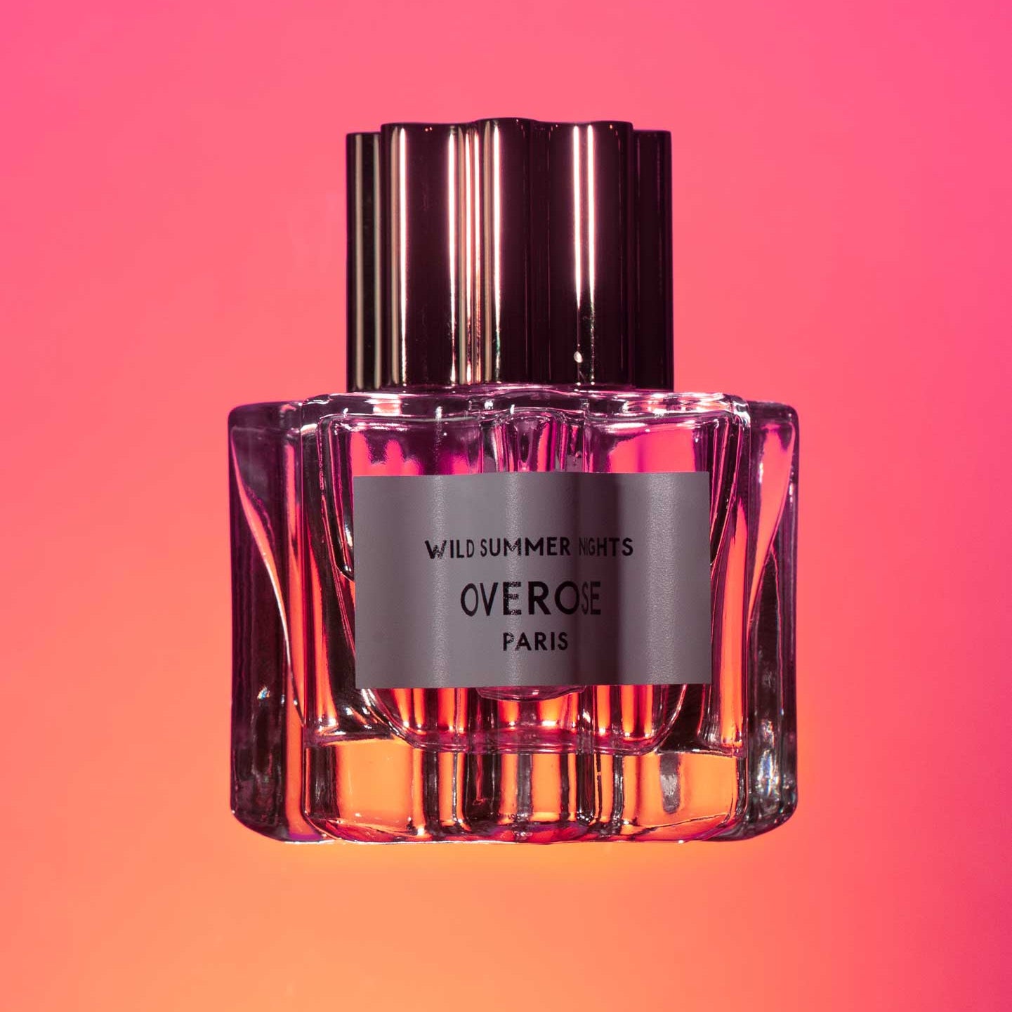 Perfume bottle with a metallic cap on a gradient pink and orange background