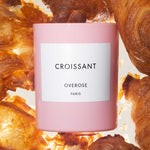 A pink candle with a white label that reads 'CROISSANT' and Croissants in the background