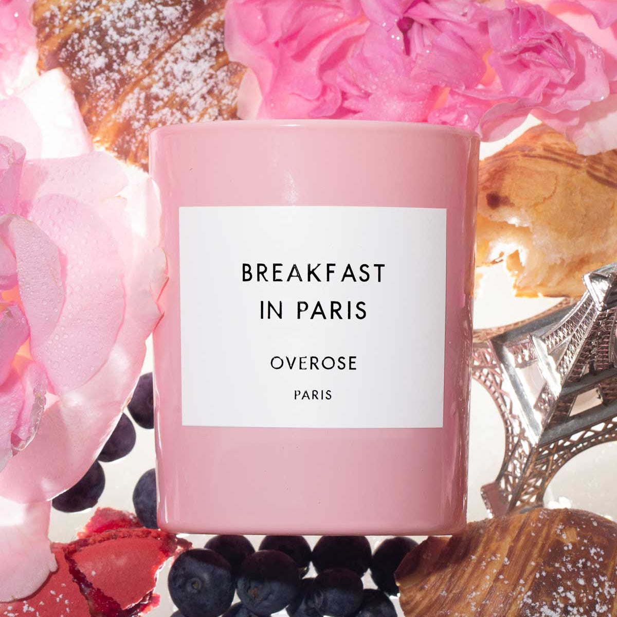 Pink 'Breakfast in Paris' candle surrounded by flowers and pastries.