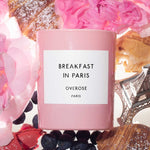 Pink 'Breakfast in Paris' candle surrounded by flowers and pastries.
