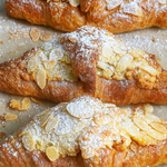 Three croissants with powdered sugar and almonds on a baking sheet.