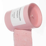 A pink scented candle with the label 'MARSHMALLOW EXTRAIT' on the front on top of a pink marshmallow