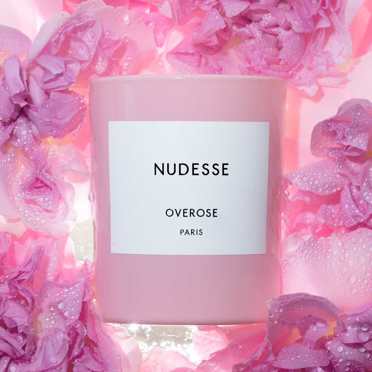 Pink candle labeled 'Nudesse' surrounded by pink roses.