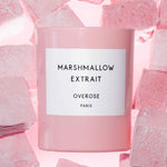 A pink scented candle with the label 'MARSHMALLOW EXTRAIT' on the front and pink marshmallows in the background