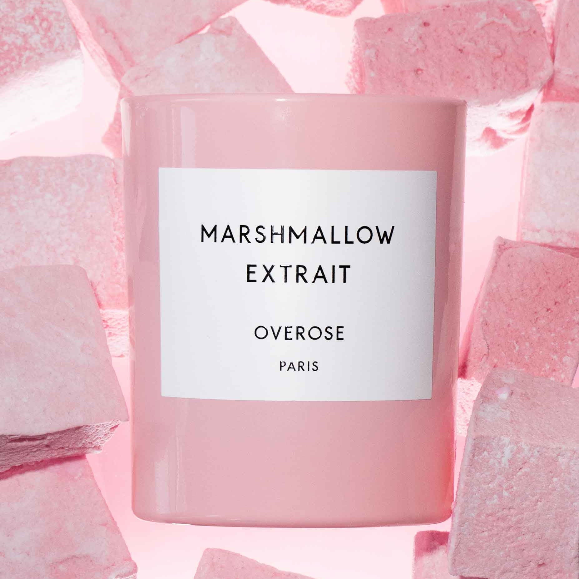 A pink scented candle with the label 'MARSHMALLOW EXTRAIT' on the front and pink marshmallows in the background