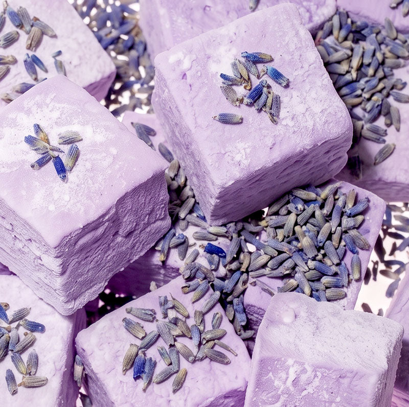 Lavender-colored marshmallows,  arranged in a pile with dried lavender buds scattered on top.