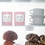 a shelf of "Cappuccino" candles, white cups, croissants and babkas
