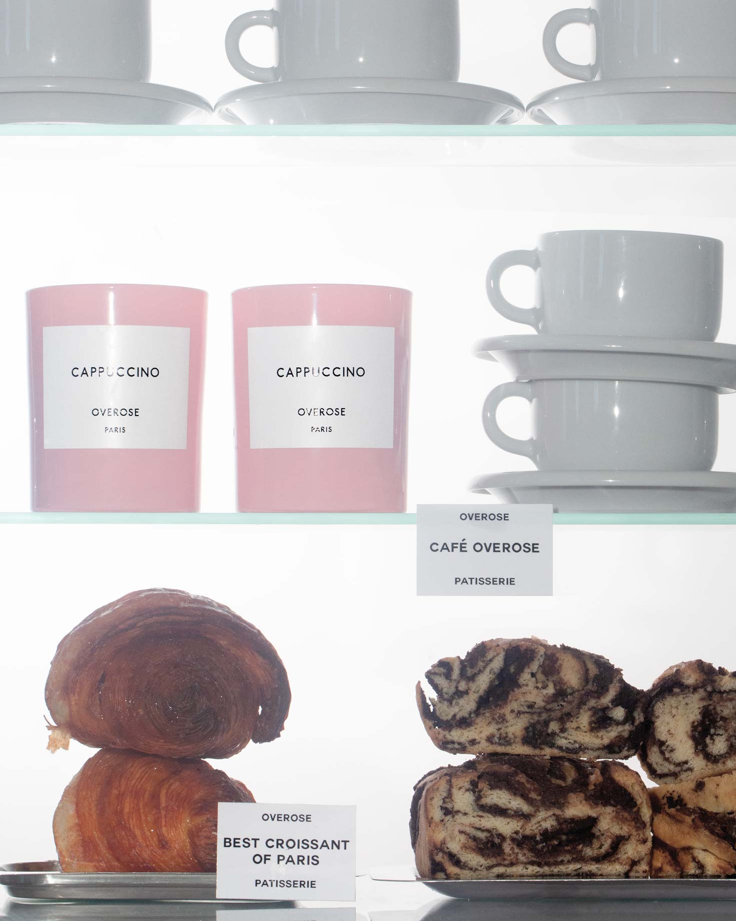 a shelf of "Cappuccino" candles, white cups, croissants and babkas