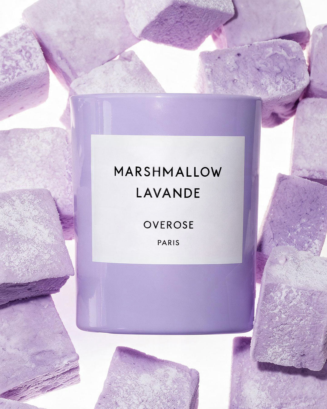 A lavender-colored candle jar labeled 'MARSHMALLOW LAVANDE OVERROSE PARIS' surrounded by lavender-colored sugar cubes on a white background.