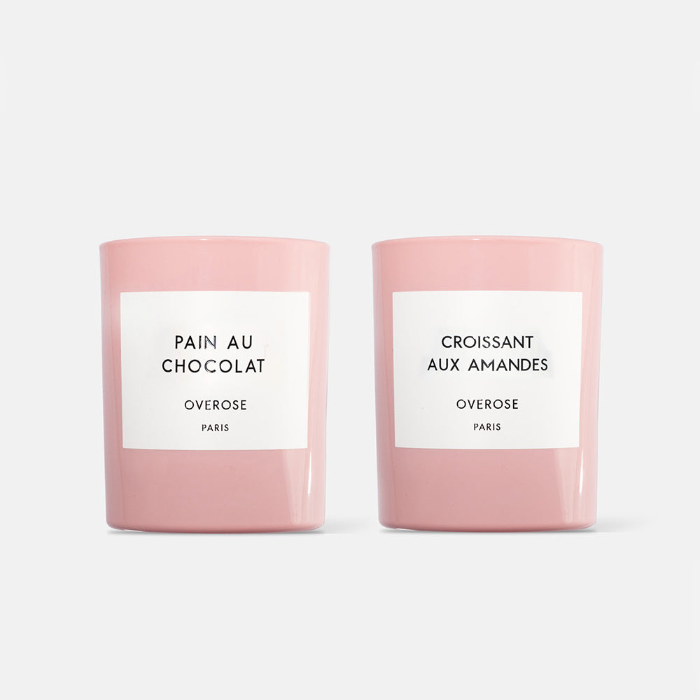 two pink candles with white labels on white background. one candle is "Pain au Chocolate" and the other is "Croissant aux Amandes"