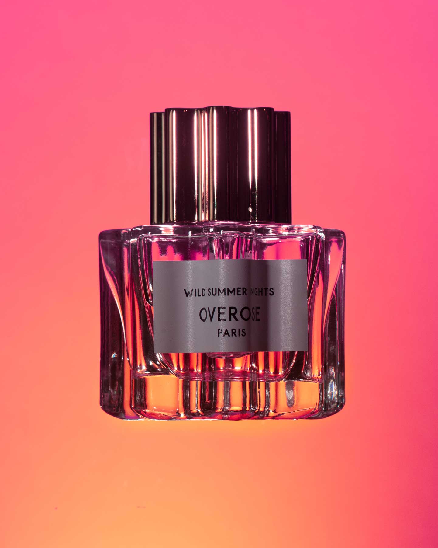 Perfume bottle with a metallic cap on a gradient pink and orange background